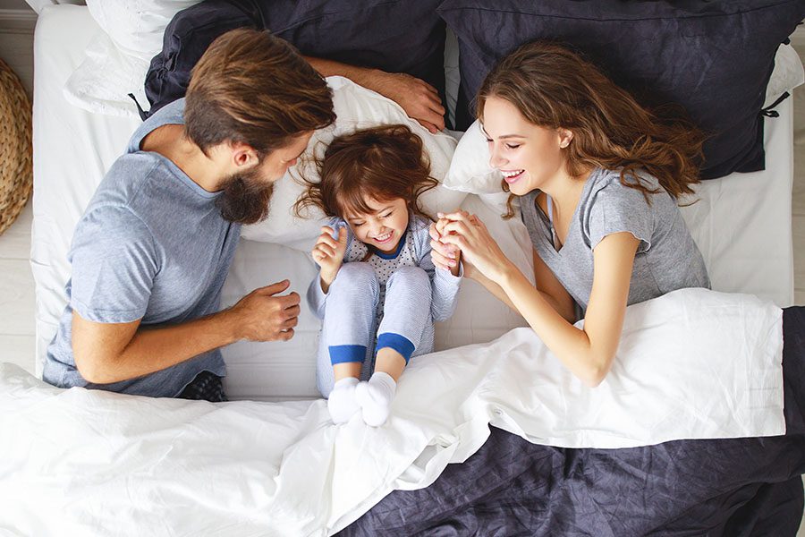 Personal Insurance - Two Young Parents Playing with Their Daughter in Bed